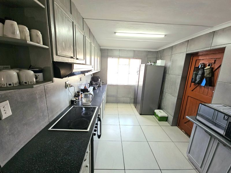 A functional galley-style kitchen featuring tiled walls, dark countertops, a built-in electric hob, extractor fan, and ample cabinetry for storage.
