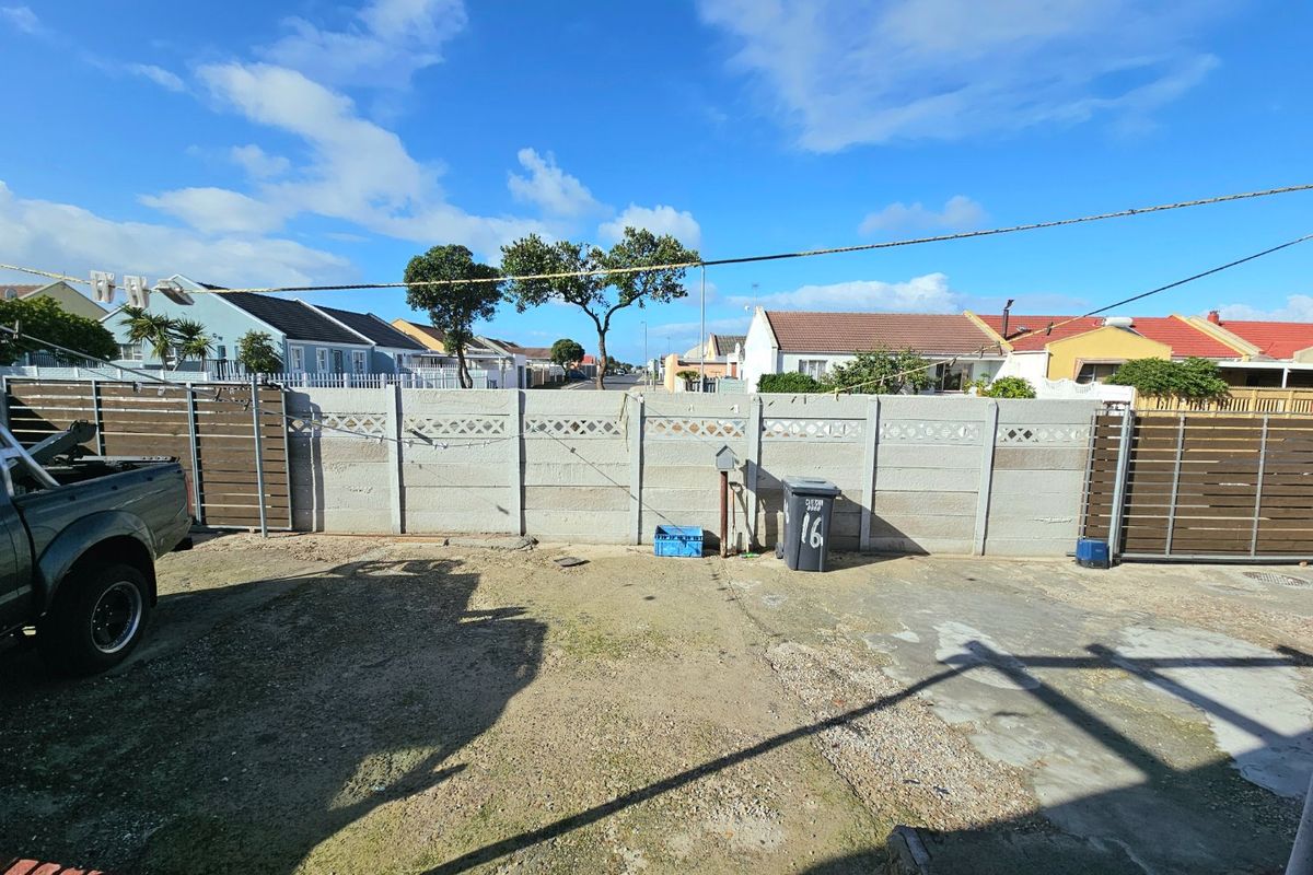 A view of the rear yard featuring a concrete driveway, perimeter precast walling, and metal gate access.