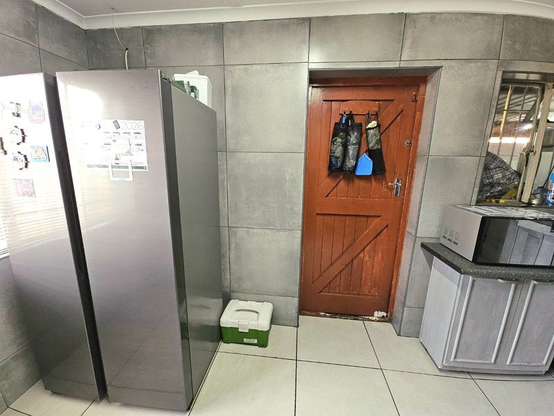A kitchen area featuring large format grey wall tiles, tiled flooring, and a wooden door leading to an exterior space.