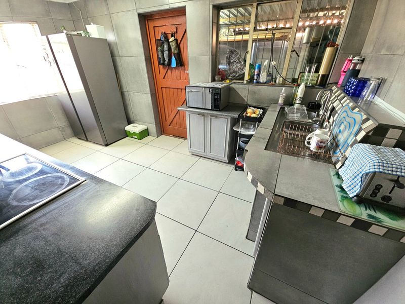 A functional kitchen featuring tiled countertops, built-in cabinetry, a sink, and a cooktop, with a direct access door to the exterior.