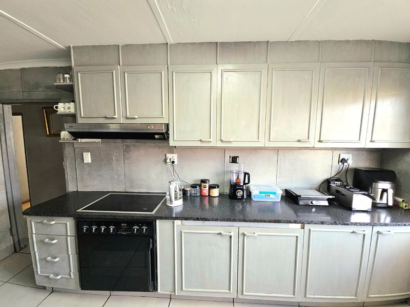 A functional kitchen featuring built-in cabinetry, a dark laminate countertop, and an integrated electric oven and hob with an extractor fan.
