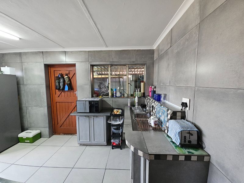 A functional kitchen featuring grey tiled walls, tiled flooring, built-in cabinetry, and a stainless steel sink with a tiled splashback.