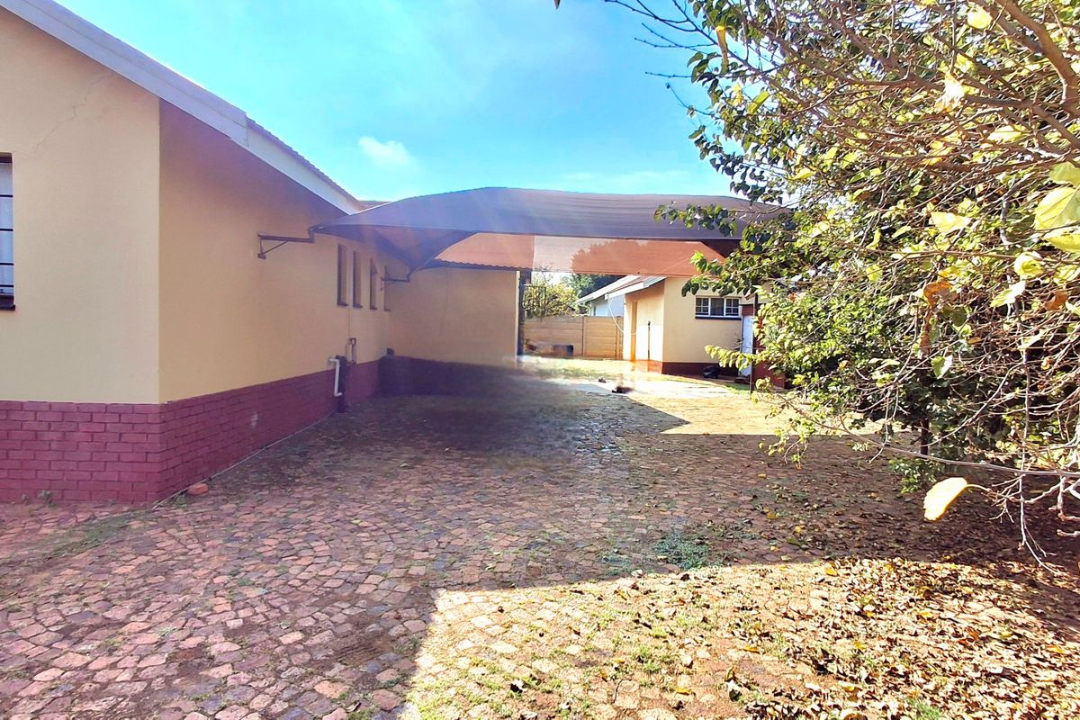Rear exterior view featuring a paved driveway, a shade cloth carport structure, and brick-plinth wall finishes.