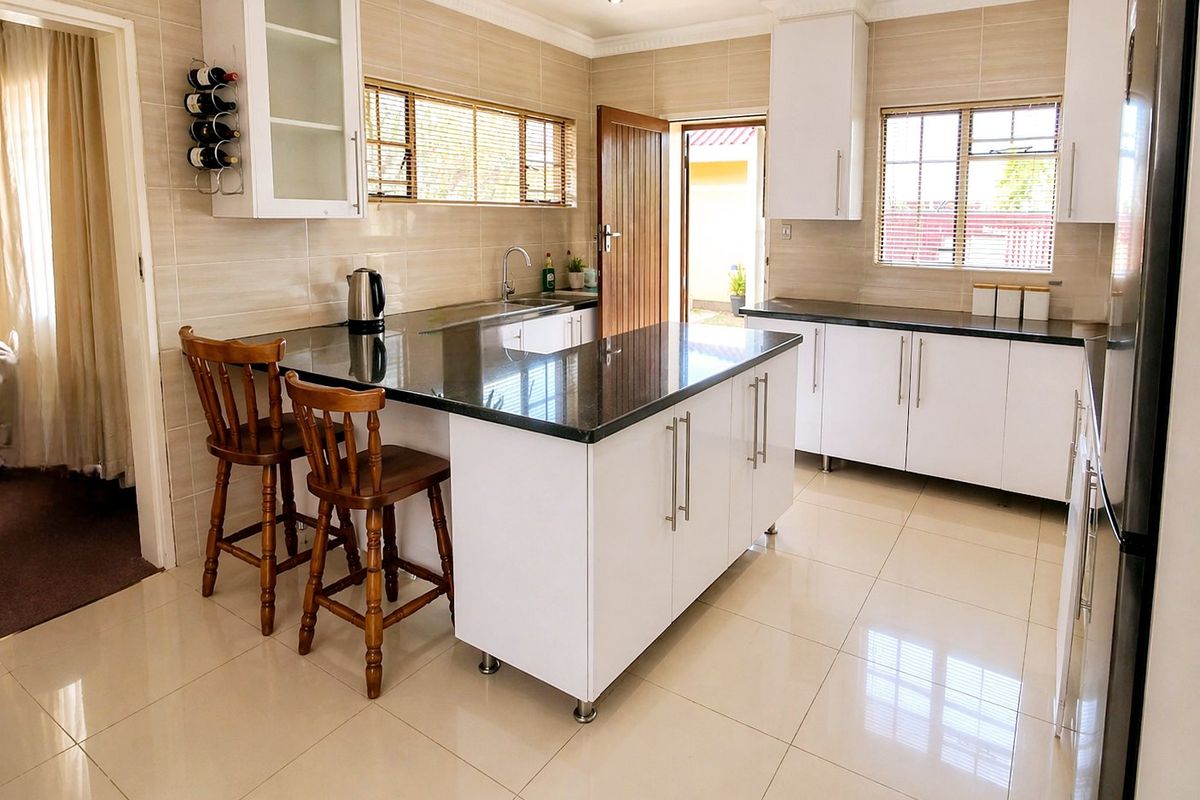 Modern kitchen featuring white cabinetry, granite countertops, a central island with breakfast bar seating, and tiled finishes throughout.