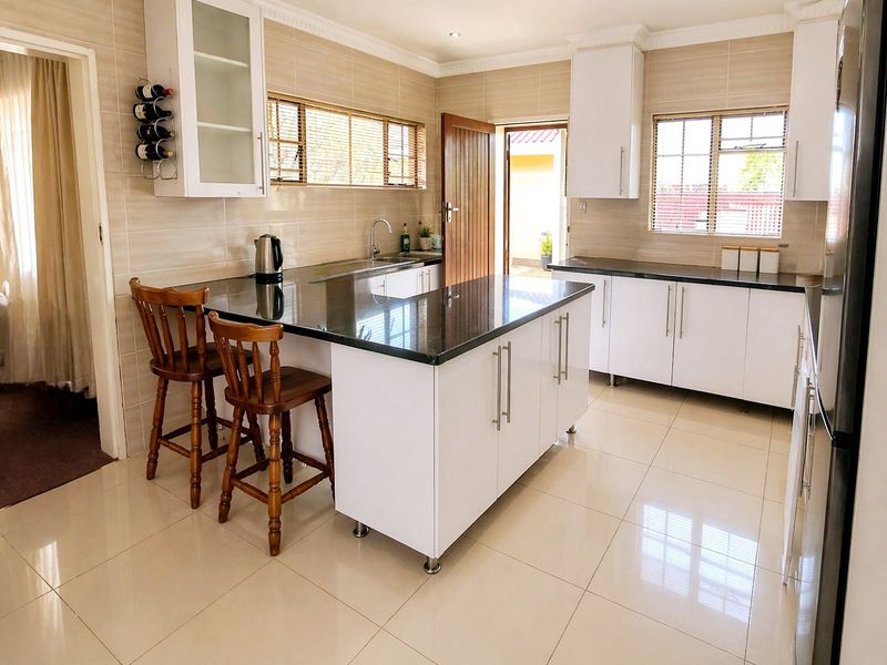 Modern kitchen featuring white cabinetry, granite countertops, a central island with breakfast bar seating, and tiled finishes throughout.