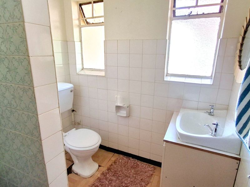 A functional bathroom featuring a standard toilet, vanity basin, and tiled wall finishes, requiring cosmetic updates to modernize the space.