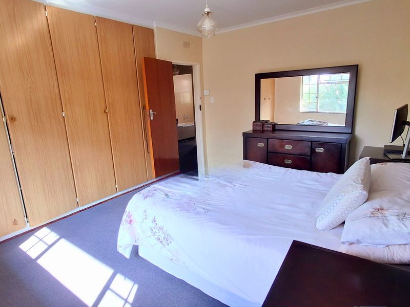 A well-lit bedroom featuring extensive built-in wooden cupboards and carpeted flooring, offering a functional and comfortable living space.
