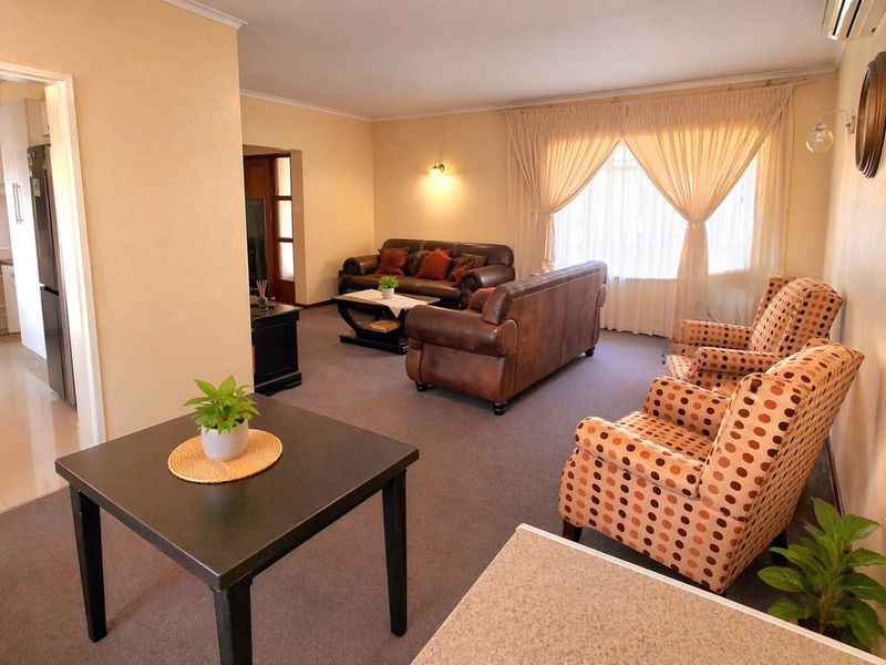 A spacious living room featuring carpeted flooring, wall-mounted air conditioning, and natural light through large windows.