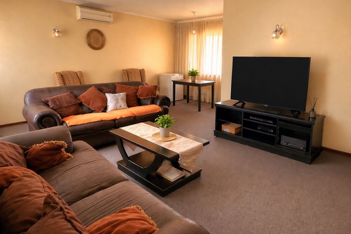 A comfortable living room featuring carpet flooring, wall-mounted lighting, and a split-system air conditioning unit.