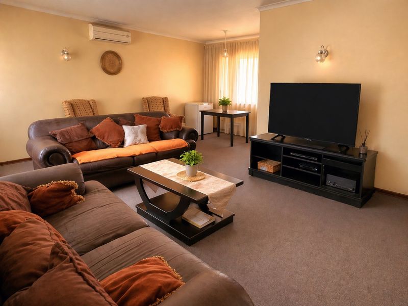 A comfortable living room featuring carpet flooring, wall-mounted lighting, and a split-system air conditioning unit.