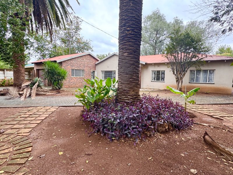 Front view of a single-story house featuring a mix of brick and plastered exterior walls, a metal roof, and a paved driveway area.