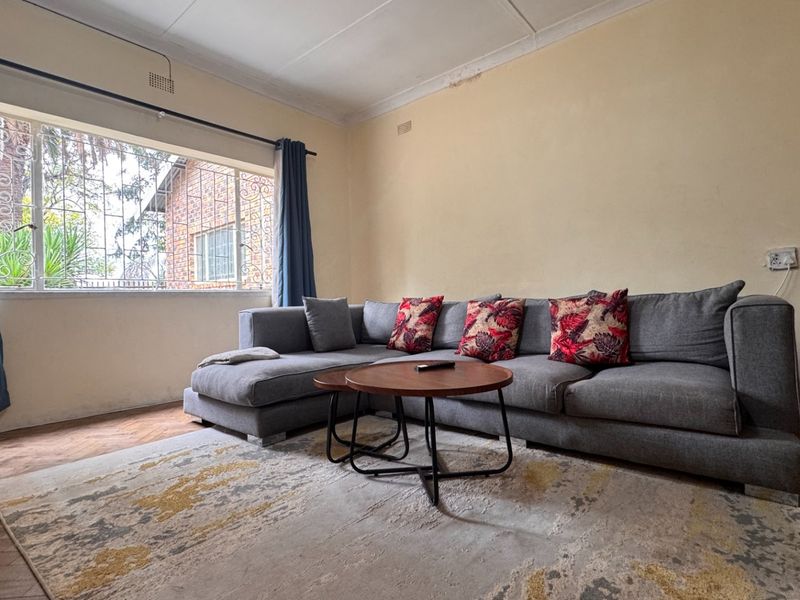 A living room featuring large windows with security bars, coved ceilings, and classic herringbone parquet flooring, offering a solid foundation for modernization.