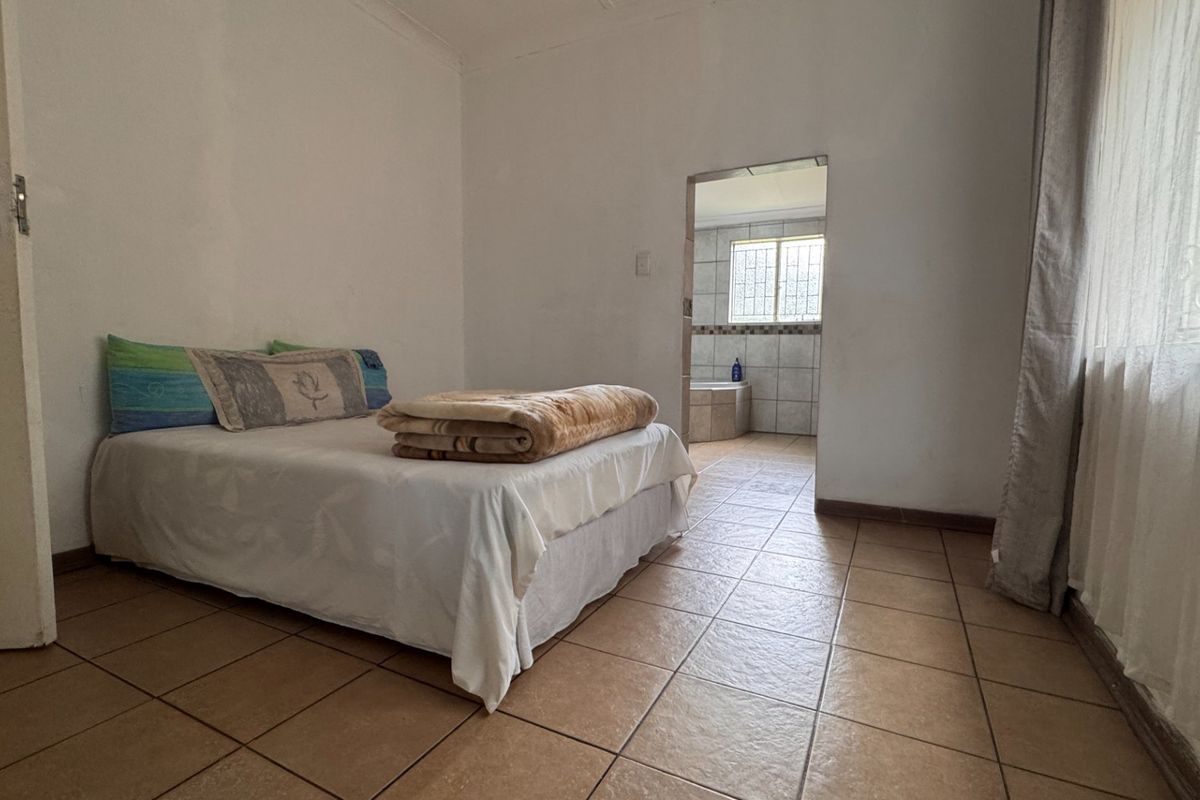 A bedroom featuring tiled flooring and direct access to an en-suite bathroom, offering a functional layout with neutral wall finishes.