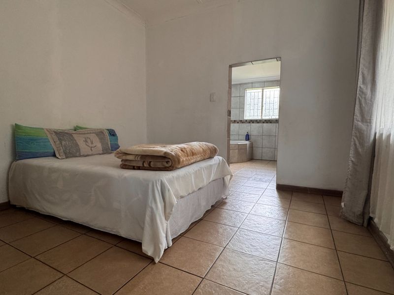 A bedroom featuring tiled flooring and direct access to an en-suite bathroom, offering a functional layout with neutral wall finishes.