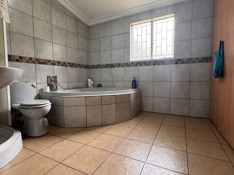 A spacious bathroom featuring a corner bathtub, pedestal basin, toilet, and floor-to-ceiling wall tiling with a decorative border.