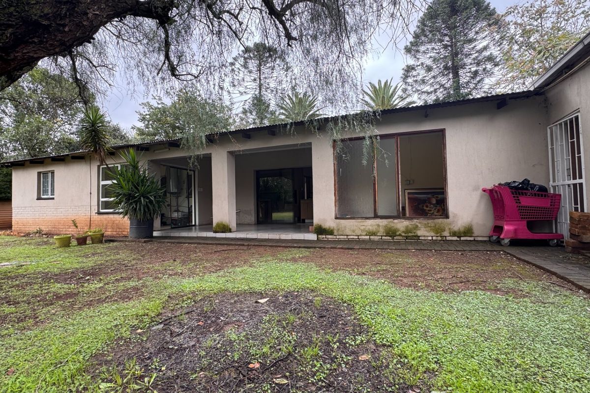 Rear view of the property featuring a covered patio area, large windows, and a spacious garden requiring landscaping and exterior maintenance.