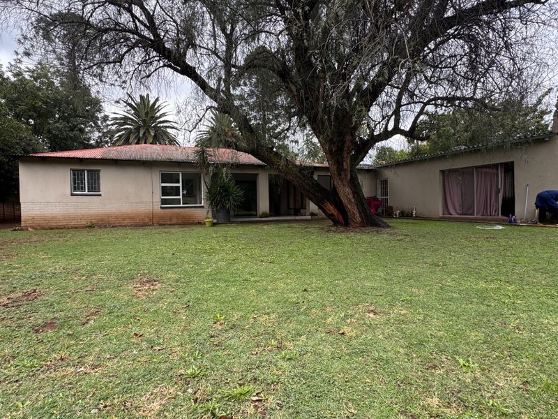 Rear view of the property featuring a large garden, mature tree, and sliding glass doors leading into the home.