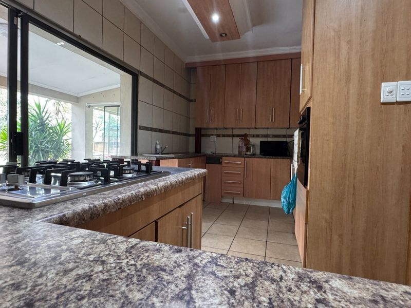 A functional kitchen featuring laminate cabinetry, granite countertops, a gas hob, and tiled finishes, with direct access to an outdoor patio area.