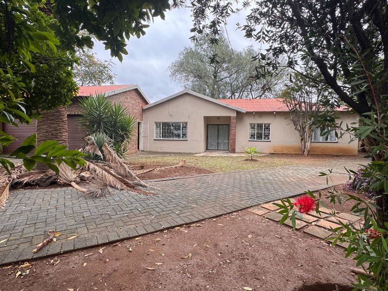 Front view of a single-story brick house featuring a paved driveway, attached garage, and security bars on the windows.