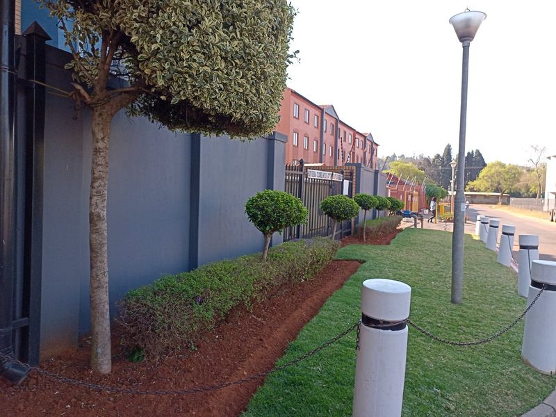 Exterior view of the apartment complex perimeter, featuring a secure boundary wall, landscaped garden beds, and paved street-side access.