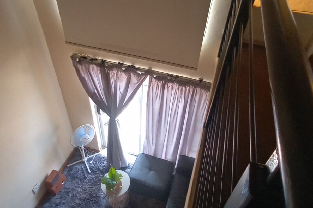 A high-angle view looking down into a living area featuring a double-volume ceiling, sliding glass doors with curtains, and a metal staircase railing.