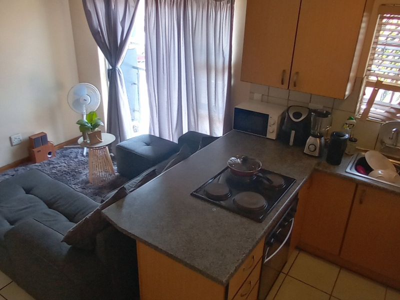 Open-plan apartment living area featuring a compact kitchen with built-in cabinetry, integrated hob, and tiled flooring, seamlessly flowing into the adjacent lounge space.