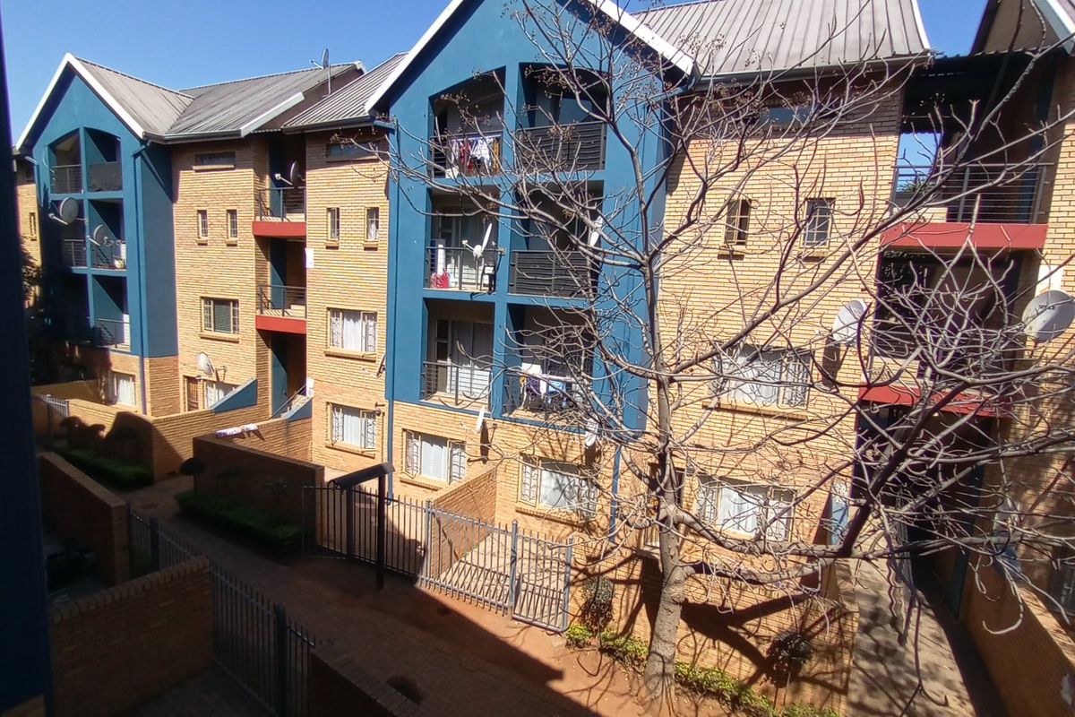 Exterior view of a multi-story apartment complex featuring face-brick facade, blue painted accents, and private balconies with metal railings.