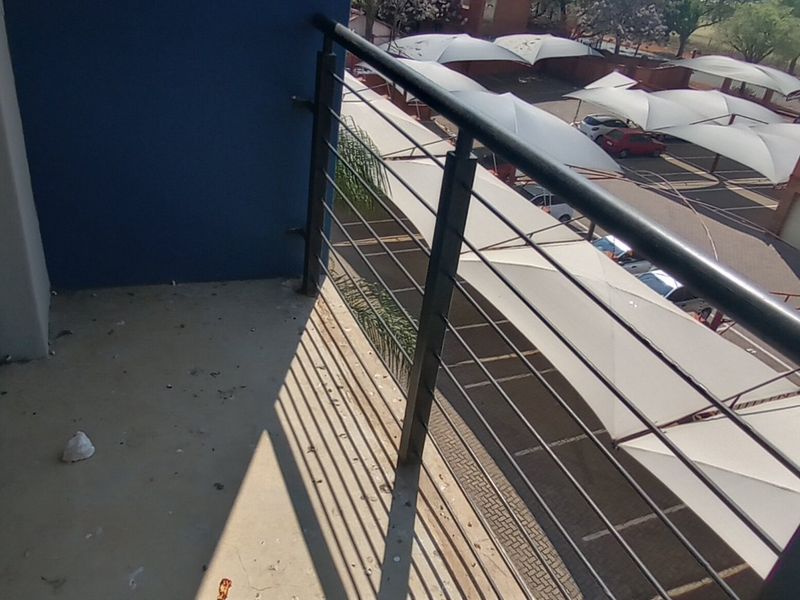 A balcony overlooking the apartment complex parking area, featuring a metal railing and concrete flooring.