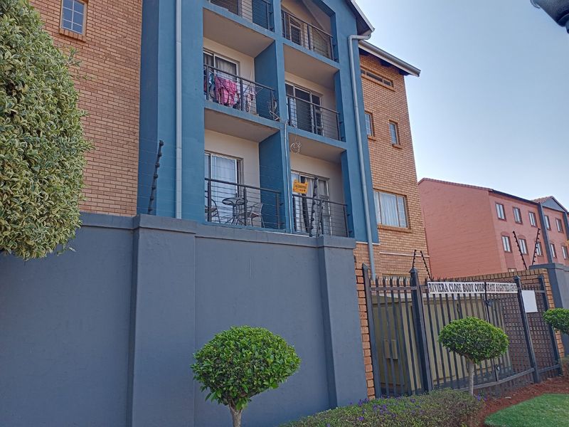 Exterior view of a multi-story apartment complex featuring brick and blue painted facade, private balconies, and secure perimeter fencing.
