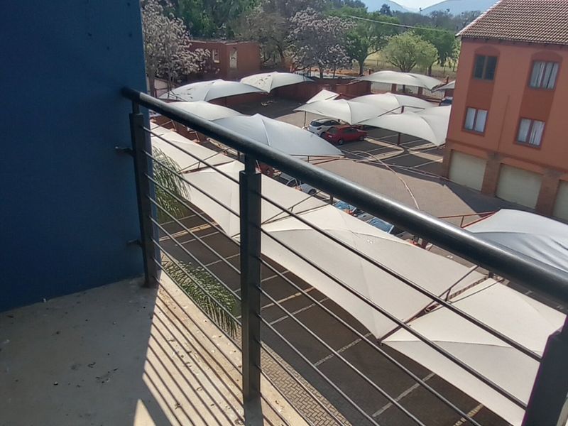 A balcony overlooking a parking area with shade cloth structures and adjacent apartment buildings.