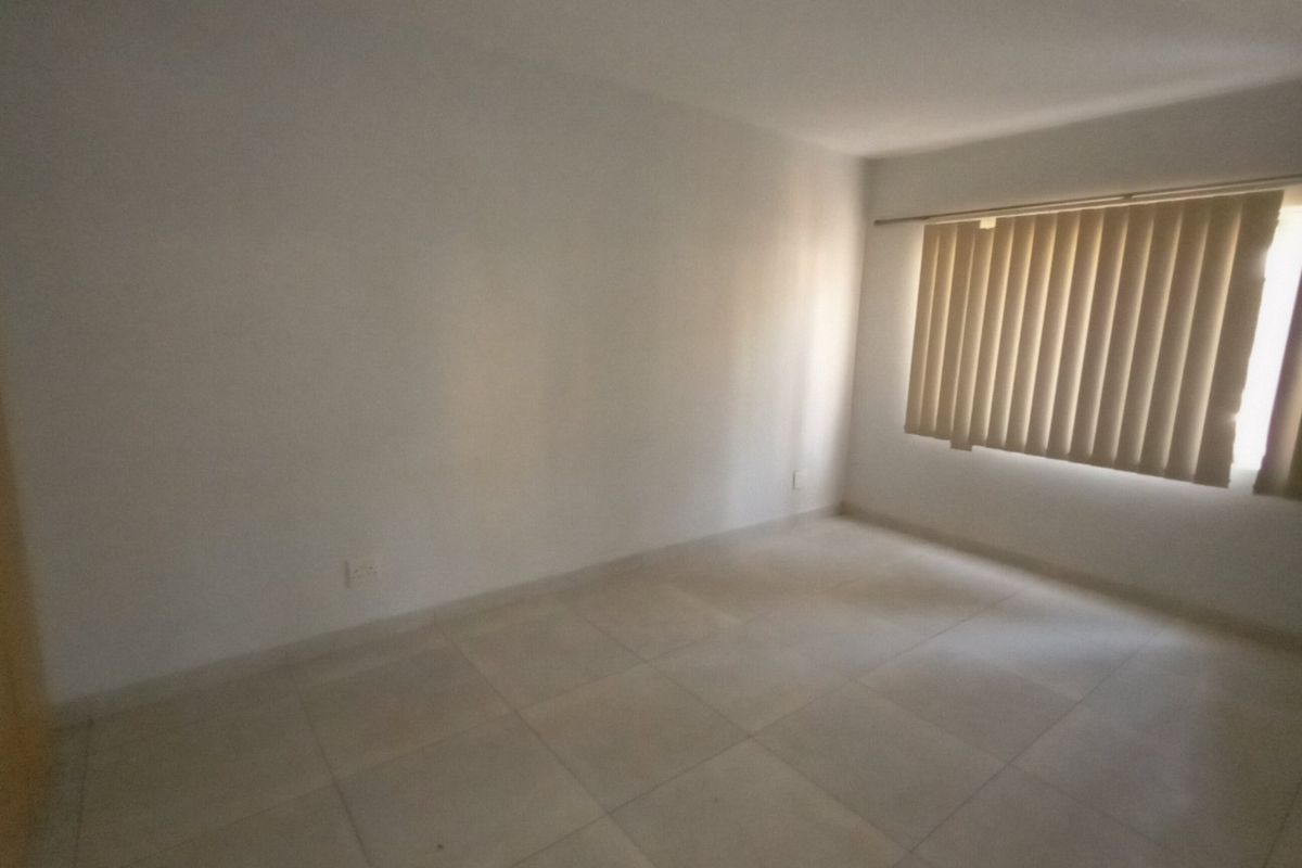 A bright, empty bedroom featuring neutral tiled flooring and vertical window blinds, offering a clean and versatile space ready for personalization.