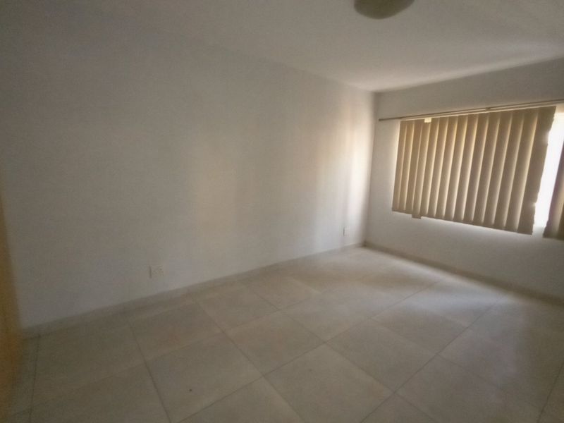 A bright, empty bedroom featuring neutral tiled flooring and vertical window blinds, offering a clean and versatile space ready for personalization.
