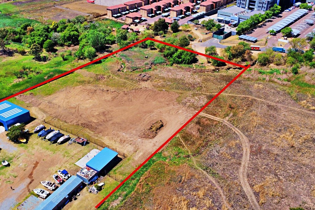 Aerial view of a vacant residential land plot with existing metal storage structures and perimeter fencing.