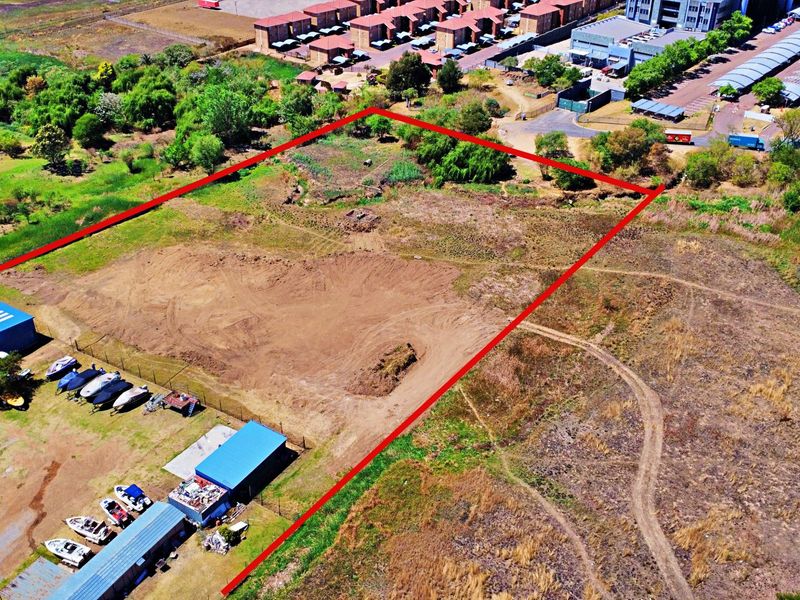 Aerial view of a vacant residential land plot with existing metal storage structures and perimeter fencing.