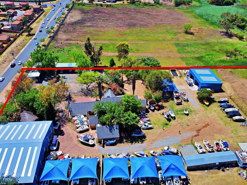 Aerial view of a residential property featuring multiple storage sheds, shade cloth carports, and extensive open yard space.