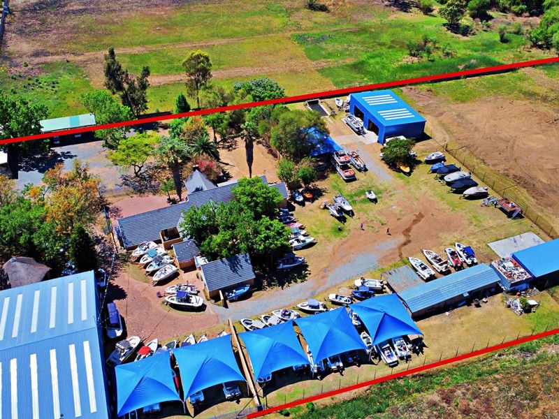Aerial view of a large residential land plot featuring multiple storage sheds, shaded parking structures, and extensive open space.