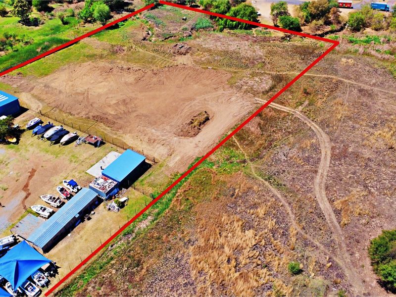 Aerial view of a vacant residential land plot featuring cleared ground, perimeter fencing, and existing metal storage structures.