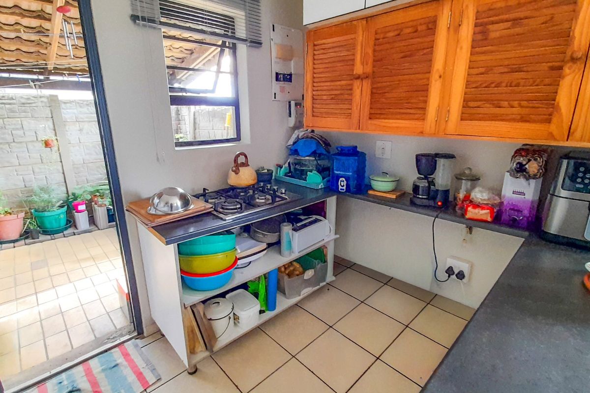 Compact kitchen area featuring a gas hob, wooden wall-mounted cabinetry, and tiled flooring with direct access to an outdoor patio area.