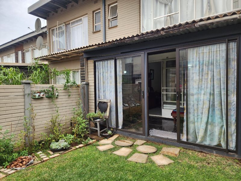 Rear exterior view of the apartment featuring a small garden, paved stepping stones, and sliding glass doors leading into the living area.