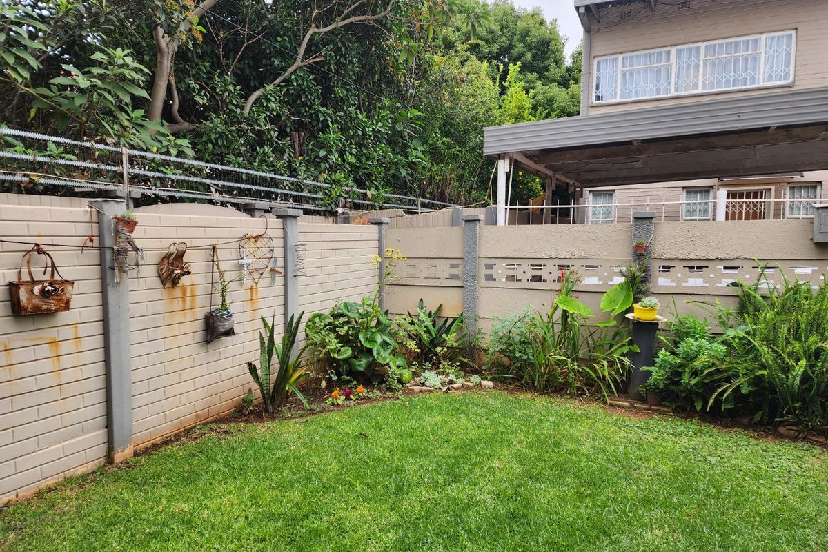 A private rear garden featuring a well-maintained lawn, established garden beds, and a secure brick boundary wall with integrated security features.