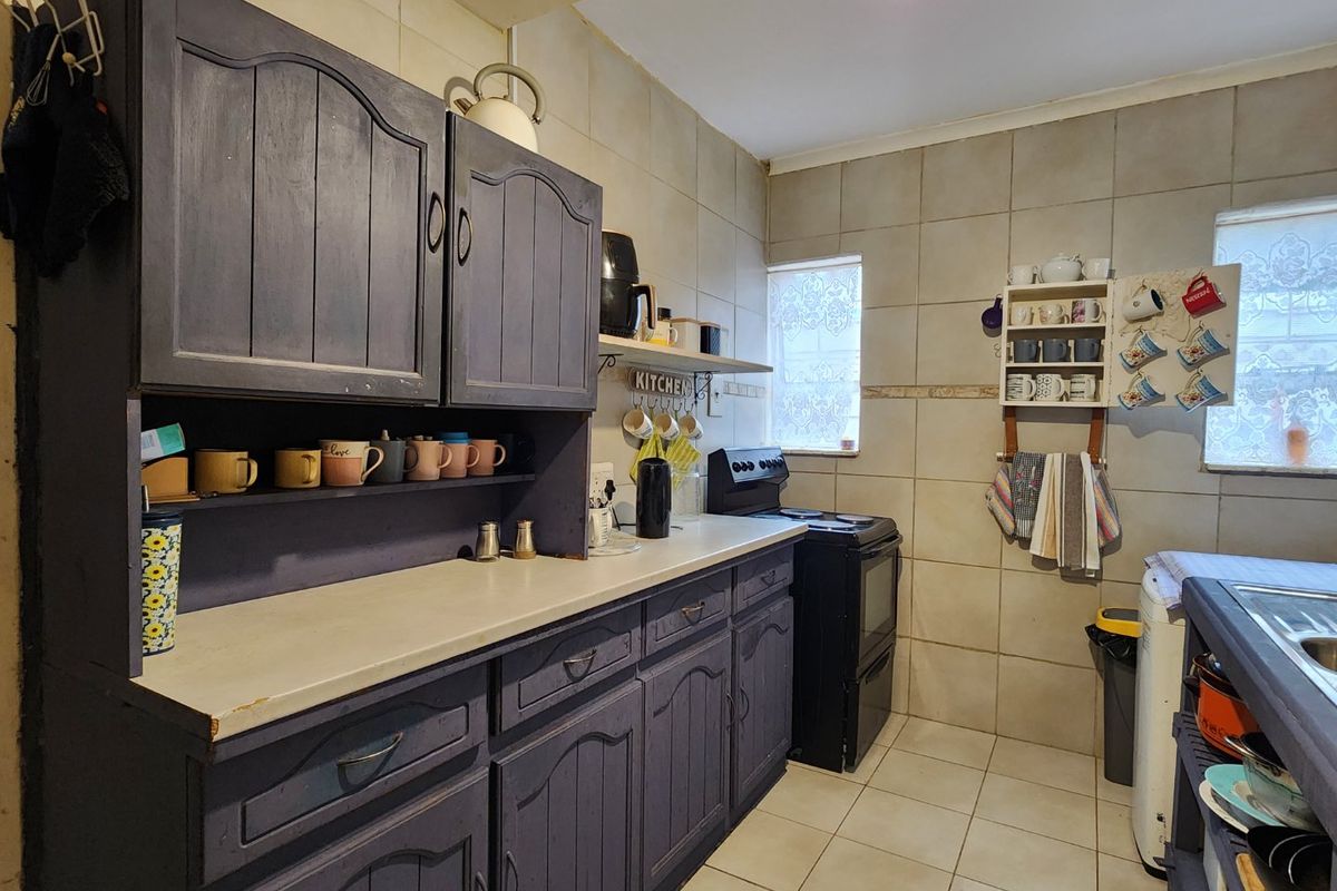 A functional kitchen featuring dark painted cabinetry, tiled walls and flooring, a freestanding stove, and a double sink with ample counter space.