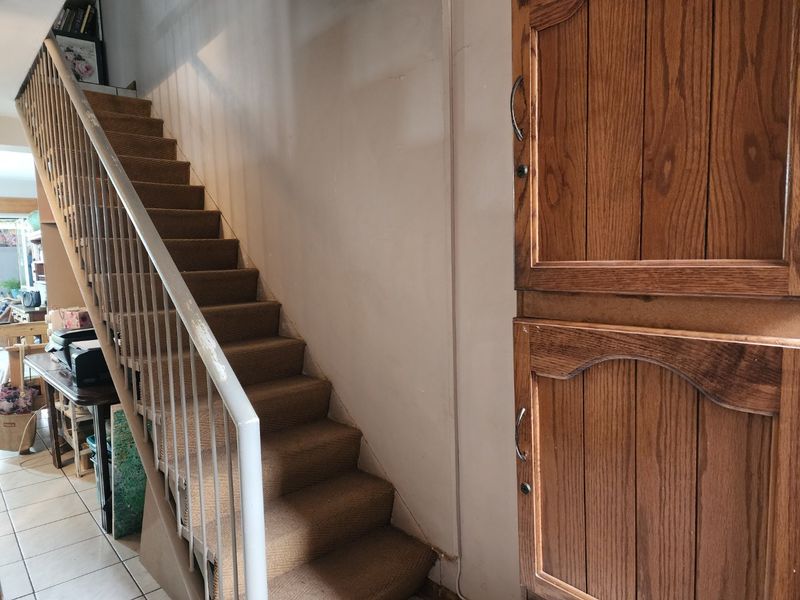 A hallway featuring a staircase with carpeted steps, a metal balustrade, and built-in wooden cabinetry providing storage space.