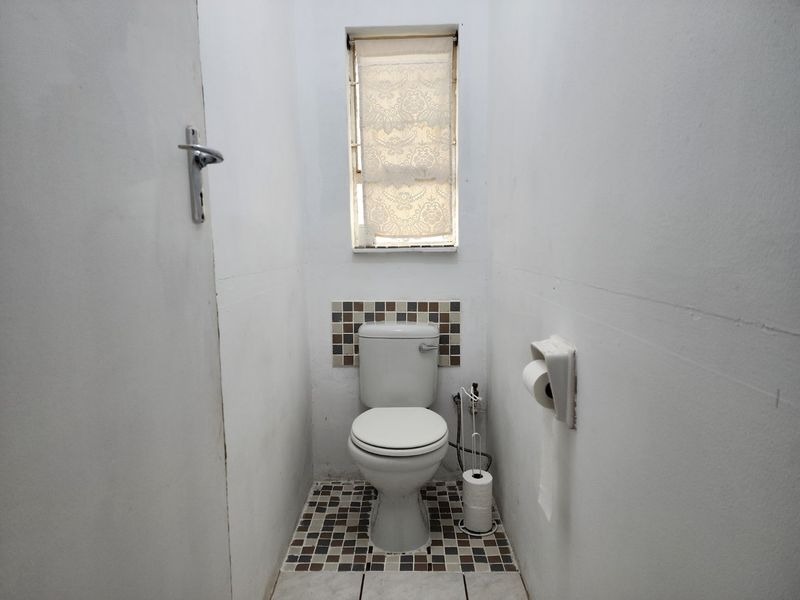 A compact guest toilet featuring mosaic tile accents on the floor and wall splashback, with a small window for natural light.