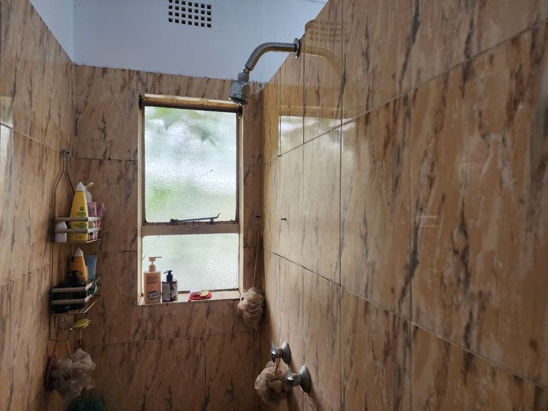 A dated shower enclosure featuring marble-effect wall tiles and an obscured glass window with integrated ventilation.