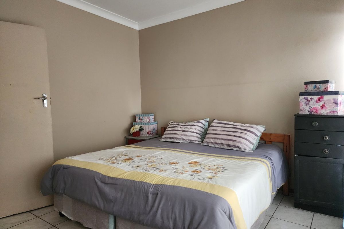 A functional bedroom featuring tiled flooring, a ceiling fan, and neutral wall tones, providing a simple and practical living space.