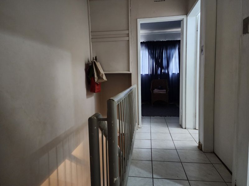 A functional hallway featuring tiled flooring, a metal balustrade, and a built-in storage cupboard, leading towards an adjacent room.