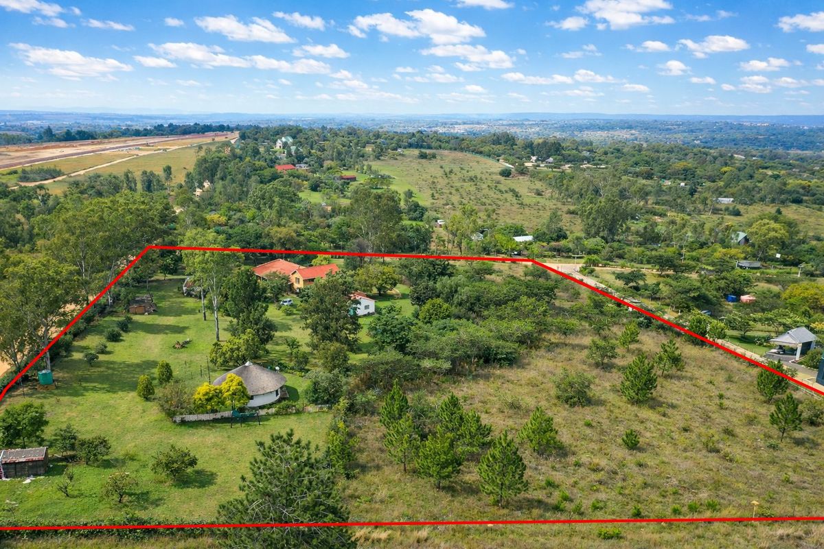 Aerial view of a large farm property featuring multiple structures, mature trees, and expansive open land within a clearly marked boundary.