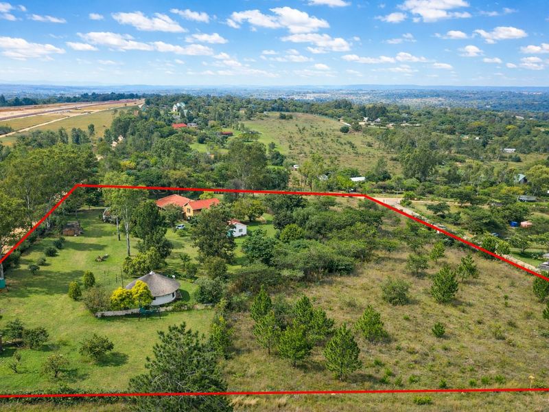 Aerial view of a large farm property featuring multiple structures, mature trees, and expansive open land within a clearly marked boundary.
