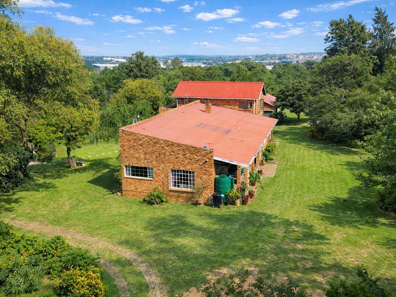 Aerial view of a brick farmhouse with a metal roof, surrounded by expansive green lawns and mature trees in a rural setting.
