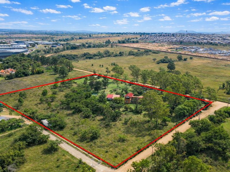 Aerial view of a large, fenced farm property featuring mature trees and established vegetation, situated in a semi-rural landscape.